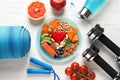 Plate with heart-healthy products and sports equipment on wooden background,