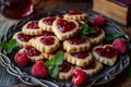 A plate of heart-shaped cookies with raspberry jam on top. The cookies are arranged in a pile, and there are several raspberries