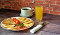 A plate of hearty breakfast, fried eggs, pancakes, croutons, tomatoes and bacon on a wooden table, next to a cup of black coffee Royalty Free Stock Photo