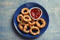 Plate with homemade crunchy fried onion rings and tomato sauce on wooden background Royalty Free Stock Photo