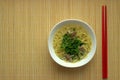 Traditional noodles with pieces of meat. A white plate lies on a straw serving napkin next to the noodle sticks