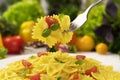 Plate of italian pasta, farfalle on fork with tomatoes and basil