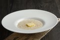 Plate of liquid oatmeal with piece of butter on wooden table