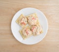Plate of lobster dip on saltine crackers atop wood table