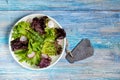 Plate with mixed fresh green salad with radish and empty slate sign, top view