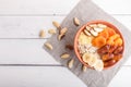 A plate with muesli, banana, dried apricots, dates, Brazil nuts on a white wooden background