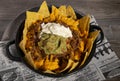 Plate of nachos with chili, sour cream guacamole and cheddar sauce on wooden table. Isolated image