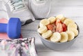 Oatmeal porridge with fresh strawberries and banana slices, a blue dumbbell, a sports top on, sneakers on a white wooden Royalty Free Stock Photo