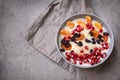 Plate of oatmeal porridge with fruit slices, tangerine slices, raisins, dried apricots, pomegranate seeds on a gray background,