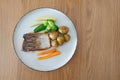 Pan-fried salmon with new potatoes, carrots, broccoli and baby sweetcorn on a wooden table is a healthy option