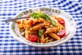 Plate with pasta pene Bolognese sauce cherry tomatoes parsley top and basil leaves on checkered blue tablecloth.