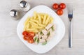 Plate with pieces chicken, pasta and tomatoes, fork