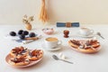 Plate with plum tarts with cinnamon and icing sugar on white wooden table, tasty puff pastry dessert.