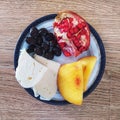 On the plate are pomegranate, cheese, peach and olive kernels