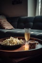 Plate of popcorn and tall glass of sparkling wine on a wooden tray. Comfy home sofa in the background.