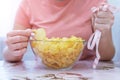 A plate of potato chips and a centimeter tape in the girl`s hands. Junk food. The concept of struggle against excess weight.