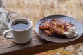 A plate of potato pancakes with sour cream and a mug of hot coffee stand on the wooden railing of the gazebo. Royalty Free Stock Photo