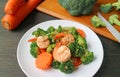 Plate of prawn stir fried with broccoli and carrot with blurry cut vegetables in background