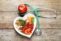 Plate with products for heart-healthy diet, apple and stethoscope on wooden background