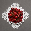 Plate with red cherries on a lacy napkin on a gray background, top view Royalty Free Stock Photo