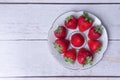 Red ripe strawberries in a plate on white wooden boards
