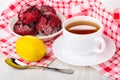 Plate with red cookies, lemon on napkin, cup of tea on saucer, spoon on table Royalty Free Stock Photo