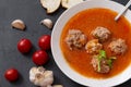 Plate of red tomato soup with meatballs, garlic and cilantro on a black background top view, fresh cherry