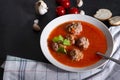 Plate of red tomato soup with meatballs, garlic and cilantro on a black background, towel