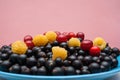 Plate with ripe berries yellow raspberry, black currant, red cherry on pink background with copy space. Royalty Free Stock Photo