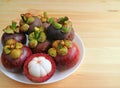 Plate of Ripe Mangosteen Whole Fruits with One Cut in Half Isolated on Wooden Table