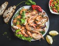 Plate of roasted tiger prawns and octopus pieces with fresh leek, salad, peppers, lemon, bread, pesto sauce over black Royalty Free Stock Photo