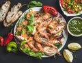 Plate of roasted tiger prawns and octopus pieces with fresh leek, salad, peppers, lemon, bread, pesto sauce over black Royalty Free Stock Photo