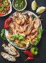 Plate of roasted tiger prawns and octopus pieces with fresh leek, salad, peppers, lemon, bread, pesto sauce over black Royalty Free Stock Photo