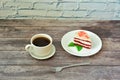 A plate with a slice of red velvet cake with mint leaves and a cup of black coffee on a light wooden table Royalty Free Stock Photo