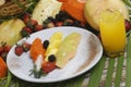 Plate of sliced pineapple, papaya, melon, strawberries, and blackberries with fruits on a table
