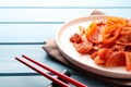 Plate of spicy cabbage kimchi with chili pepper and chopsticks on light blue wooden table, closeup Royalty Free Stock Photo