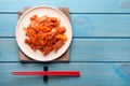 Plate of spicy cabbage kimchi with chili pepper and chopsticks on light blue wooden table, flat lay. Space for text Royalty Free Stock Photo