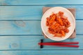 Plate of spicy cabbage kimchi with chili pepper and chopsticks on light blue wooden table, flat lay. Space for text Royalty Free Stock Photo