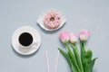 A plate with a sweet doughnut with pink icing next to a Cup of coffee, a bouquet of pink tulips, paper tubes. Spring women`s Royalty Free Stock Photo