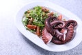 Plate with tasty boiled octopus tentacles and salad on grey textured table, closeup Royalty Free Stock Photo