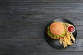 Plate with tasty burger, french fries and sauce on wooden background, top view. Royalty Free Stock Photo