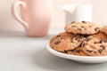 Plate with tasty chocolate chip cookies and blurred cup of milk on gray background Royalty Free Stock Photo