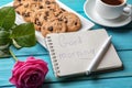 Plate with tasty chocolate chip cookies, cup of coffee and GOOD MORNING note in notebook on color wooden table Royalty Free Stock Photo