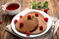 Plate with tasty chocolate pancakes, raspberries and cup of tea on wooden table