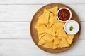 Plate with tasty Mexican nachos chips and sauces on wooden table, top view. Space for text