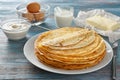 Plate with tasty thin pancakes and ingredients on wooden table