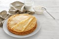 Plate with tasty thin pancakes, sour cream and jug of milk on wooden table