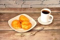 A plate with three cottage cheese buns, a cup of hot coffee on a saucer and a teaspoon on a wooden table Royalty Free Stock Photo