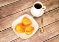 A plate with three fresh cottage cheese buns on a wooden table, next to it is a cup of black coffee and a spoon Royalty Free Stock Photo