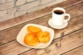 A plate with three fresh cottage cheese buns on a wooden table, next to a cup of hot black coffee Royalty Free Stock Photo
